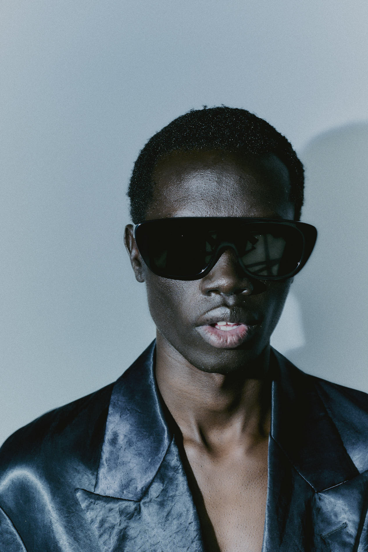 Model wearing 080 black acetate sunglasses, black satin suit jacket, minimal background