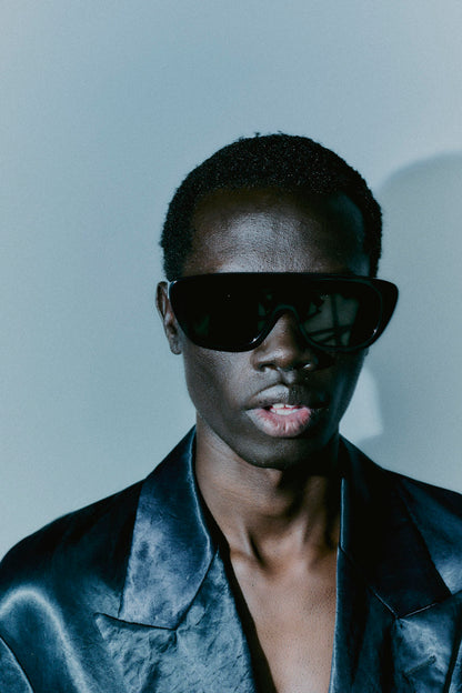 Model wearing 080 black acetate sunglasses, black satin suit jacket, minimal background